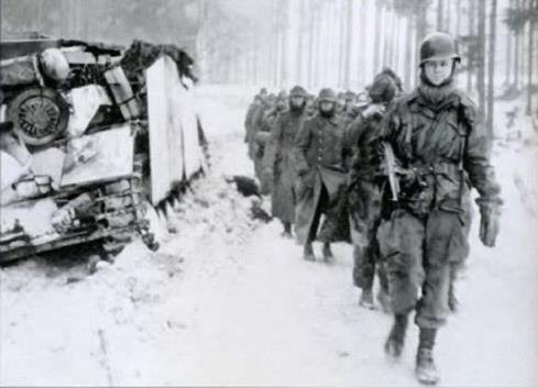 A paratrooper of the 82nd Airborne Division leads a column of German prisoners past a disabled Stug IV in the Ardennes during the Battle of the Bulge.jpg